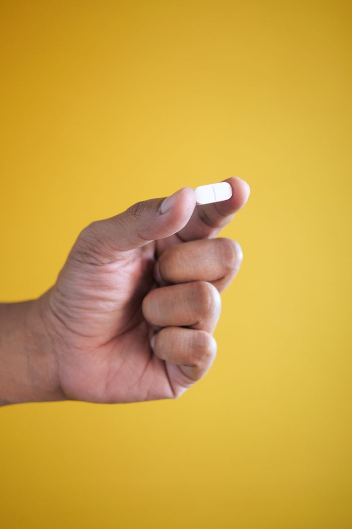 Home A hand holding a small white pill against a bright yellow background, perfect for healthcare themes.
