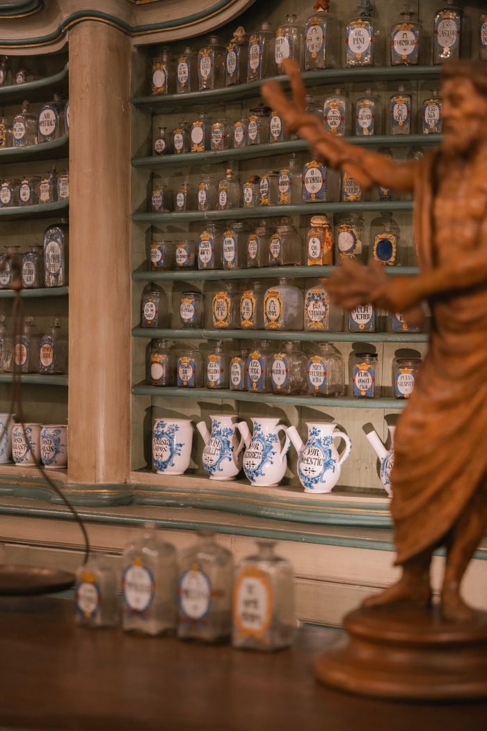 Home A historic apothecary interior showcasing antique herbal jars and a wooden statue.