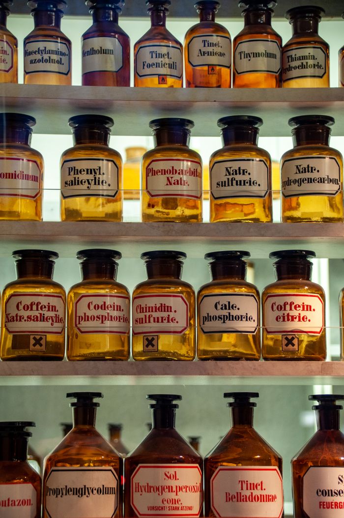 Home A collection of vintage apothecary bottles with Latin labels displayed on shelves.
